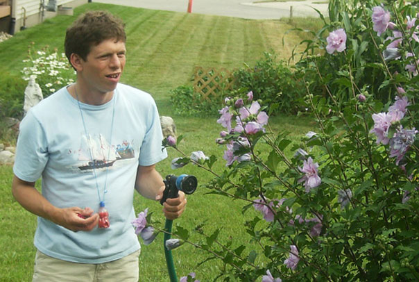 young man watering a bush of purple flowers with a hose