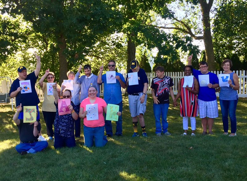 group of happy people on grass holding up drawings they've done